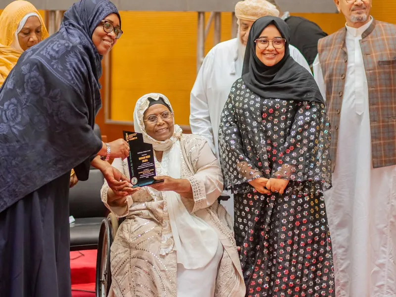 A woman in a wheelchair holds an award plaque. Women and men stand beside her on a stage.