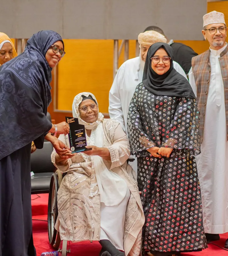 A woman in a wheelchair holds an award plaque. Women and men stand beside her on a stage.