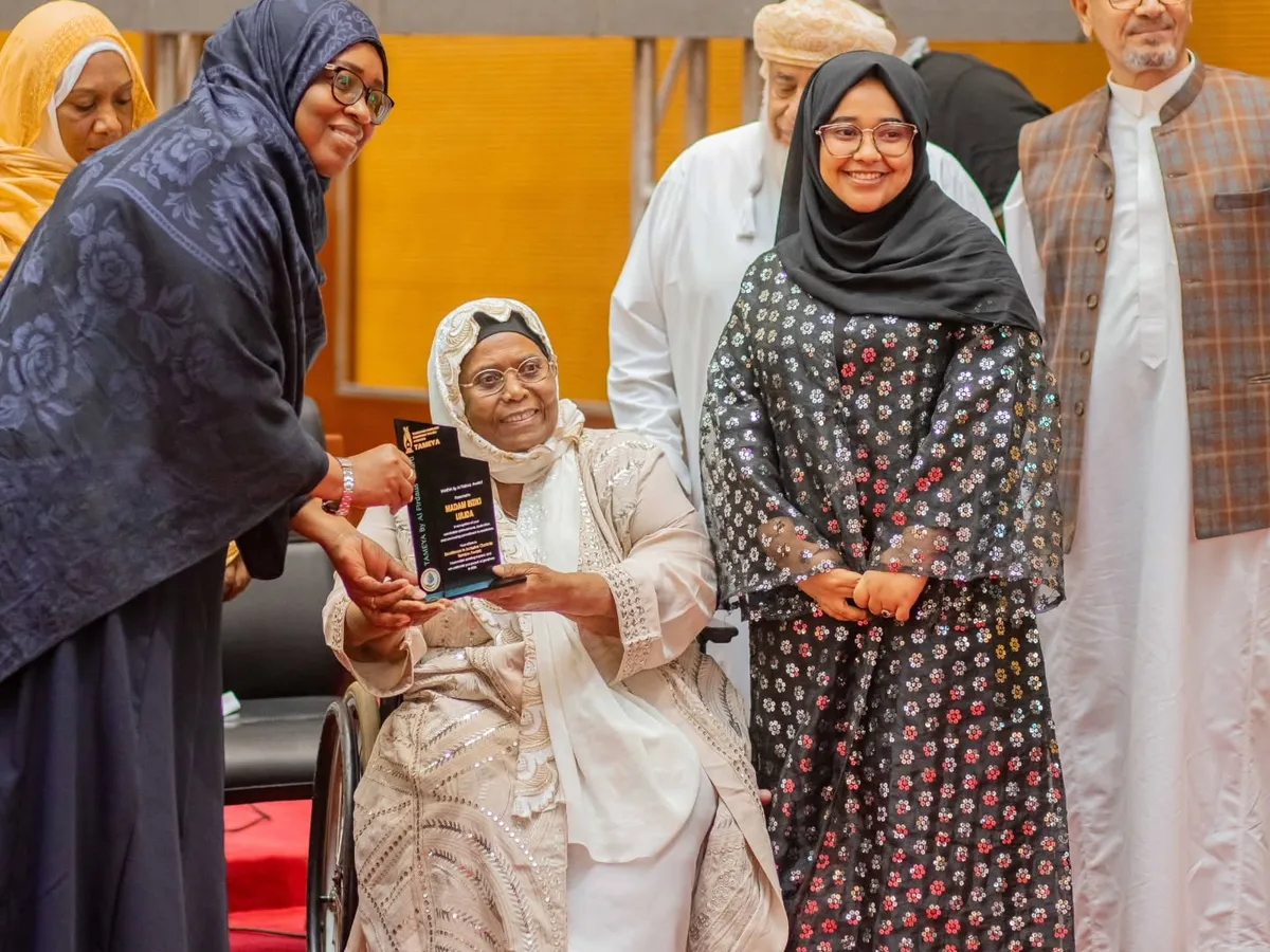 A woman in a wheelchair holds an award plaque. Women and men stand beside her on a stage.